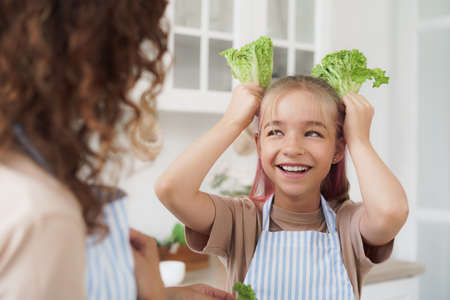 Mother and daughter playing and having fun with vegetables in kitchenの写真素材