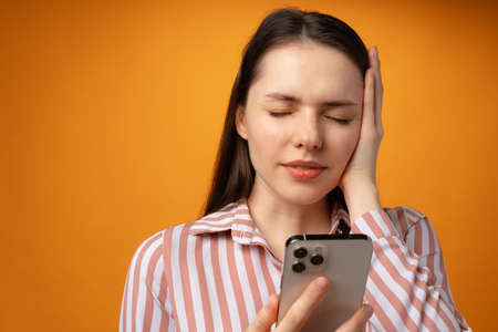 Stressed frustrated young woman holding smartphone, recieved bad news, yellow backgroundの写真素材
