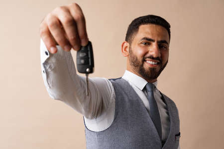 Young arab guy holding a car key and showing it against beige backgroundの写真素材