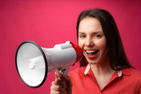 Young brunette woman shouting in megaphone against pink backgroundの写真素材