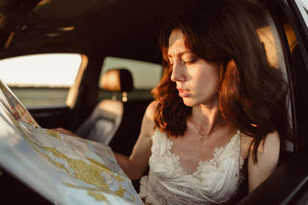 Lost young woman sitting in her car in the countryside and looking at mapの写真素材