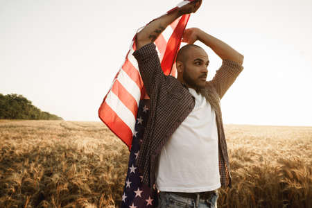 African american young man holding USA national flag through wheat fieldの写真素材