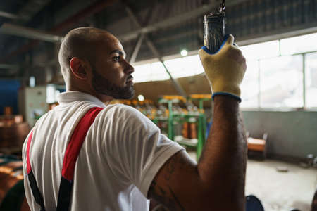 Engineer in uniform using crane controller hanging from ceiling in a factory
