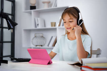 Little caucasian girl in headphones have video call distant class with teacher at homeの写真素材