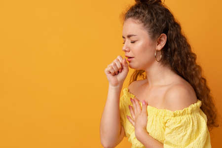 Sick young woman coughing against yellow studio backgroundの写真素材