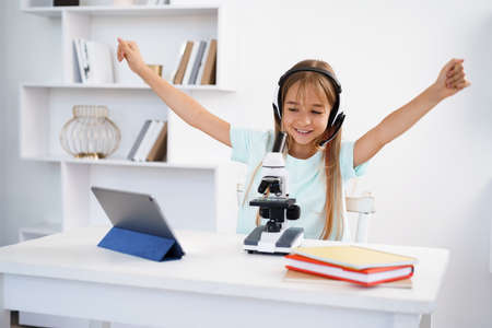 Young girl using microscope during online lesson education at home