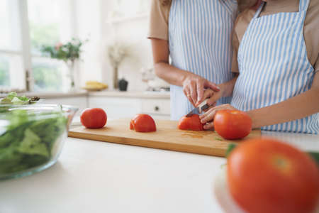 Close up of a woman and girl cutting vegetables for salad in kitchenの写真素材