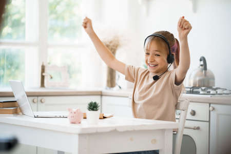 Little caucasian girl in headphones have video call distant class with teacher at homeの写真素材
