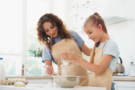 Teen girl helping her mom to cook dough in their kitchen at homeの写真素材