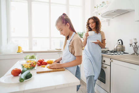 Mommy teaching her teen daughter to cook vegetable salad in kitchenの写真素材