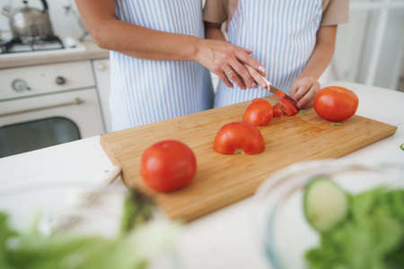 Close up of a woman and girl cutting vegetables for salad in kitchenの写真素材