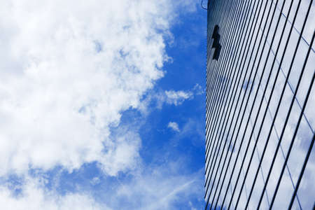 Glass skyscraper building with cloudy blue sky backgroundの写真素材