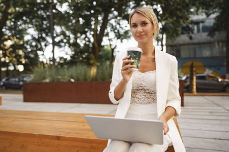 Young beautiful businesswoman working on laptop, sitting on the bench in the streetの写真素材