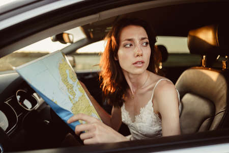 Lost young woman sitting in her car in the countryside and looking at map