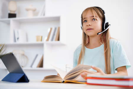 Little caucasian girl in headphones have video call distant class with teacher at homeの写真素材