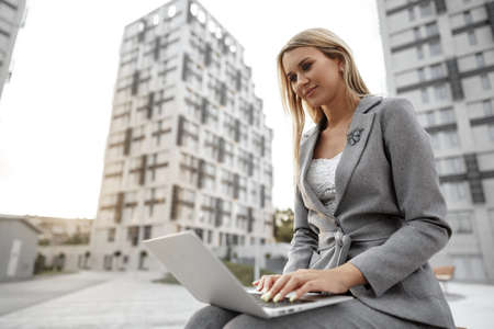 Young beautiful businesswoman working on laptop, sitting on the bench in the street