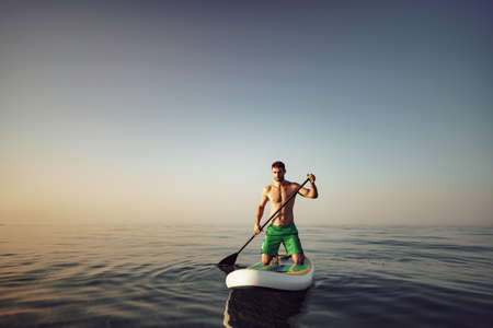 Young fit man on paddle board floating on lake.の写真素材