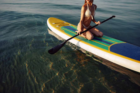 Close up of young woman sitting on a stand up paddle board