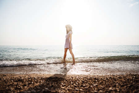 Lonely young woman walks on the seashore at sunsetの写真素材