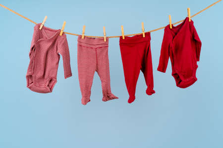 Baby girl clothes pinned on a clothesline against blue backgroundの写真素材