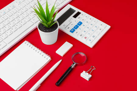 Red office desk table with blank notebook, keyboard and supplies. Top view with copy space. Flat lay.の写真素材