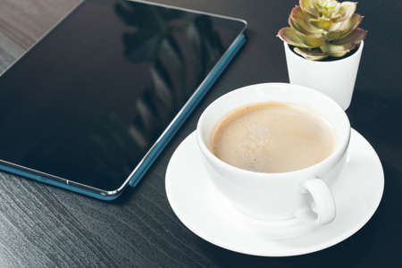 Digital tablet with black screen, coffee mug and small plant on a working tableの写真素材