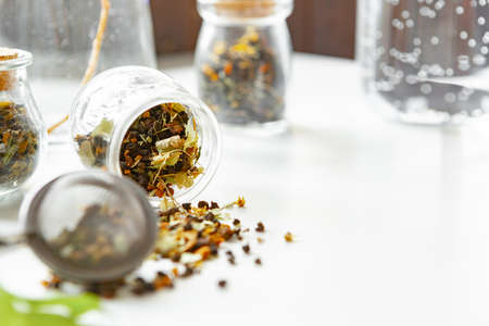 Glass jars with dry tea leaves close up on white table