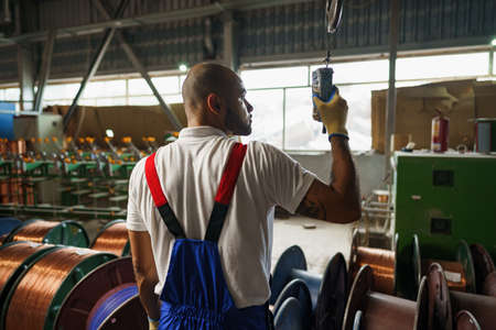 Engineer in uniform using crane controller hanging from ceiling in a factoryの写真素材