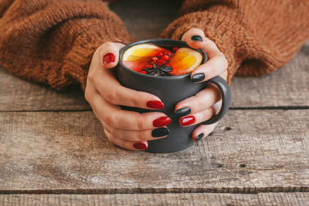 Womans hands in warm sweater holding a cup of mulled wineの写真素材