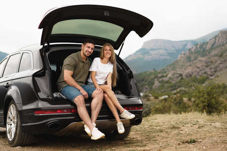 Young happy couple on a road trip sitting in car trunkの写真素材