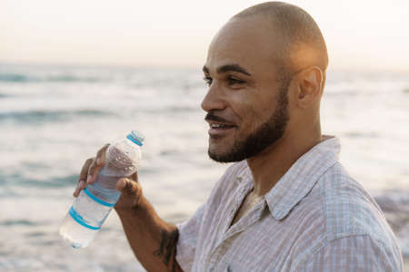 African american man drinking water from the bottle on beachの写真素材