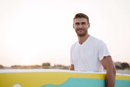 Young man carrying sup board after water surf sessionの写真素材