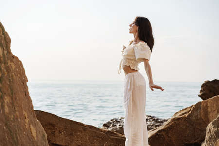 Young stylish woman standing on cliff at the sea at sunset