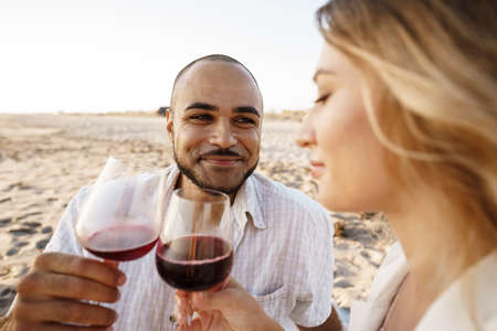 Portrait of a young couple sitting on the beach and drinking wine