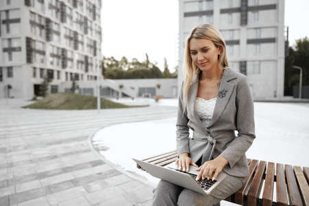 Young beautiful businesswoman working on laptop, sitting on the bench in the street