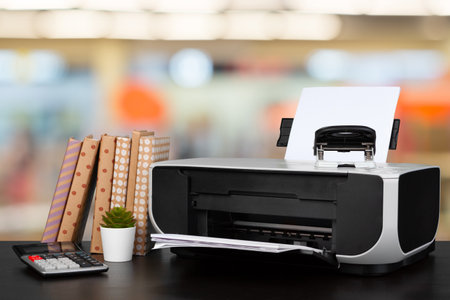 Compact home printer on desk with books against blurred backgroundの写真素材