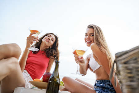 Two young female friends having picnic on a beach drinking cocktailsの写真素材