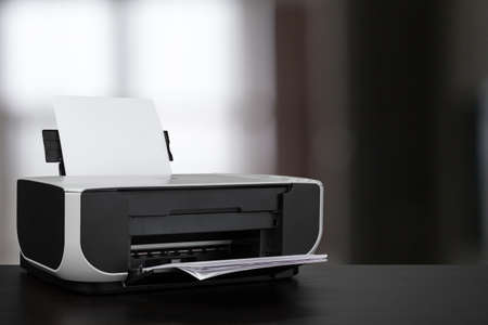 Compact laser printer on black desk against blurred background