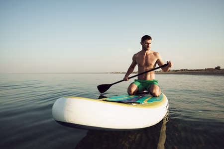 Young fit man on paddle board floating on lake.