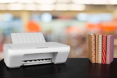 Compact home printer on desk with books against blurred backgroundの写真素材