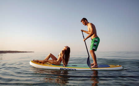 Couple of tourists young man and woman having fun paddleboarding at seaの写真素材