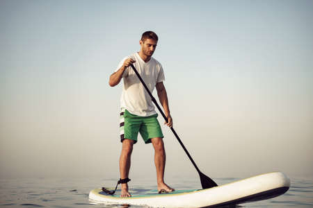 Young man in t-shirt and shorts floating on SUP boardの写真素材