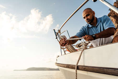 Young african american sailor tying ropes on sailboat in the sea on sunsetの写真素材