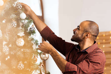 African American man decorating Christmas tree at homeの写真素材