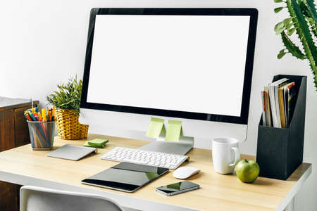 Computer monitor with mockup white screen on office table with supplies