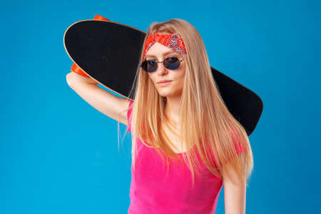 Attractive young woman holding her skateboard over blue backgroundの写真素材