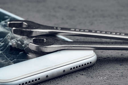 Crashed smartphone with repairing tools on grey background