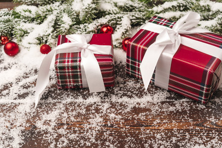 Presents on wooden background with fir tree branches and red baubles powdered with snow