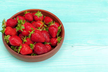 Bowl of strawberry harvest on wooden table close up