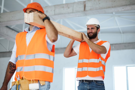 Two young men builders carrying wood planks on construction site, close upの写真素材